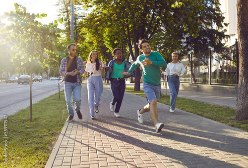 Six happy multiethnic friends meet up, have fun and enjoy free time. Diverse group of cheerful young people running on clean paved sidewalk while hanging out in beautiful summer city all together