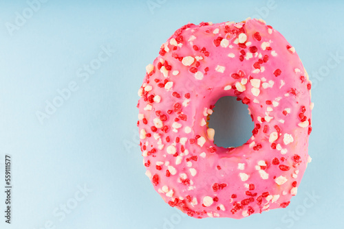 Pink sweet donut with pink sprinkles. Delicious glazed donut on blue background. Top view. Copy space