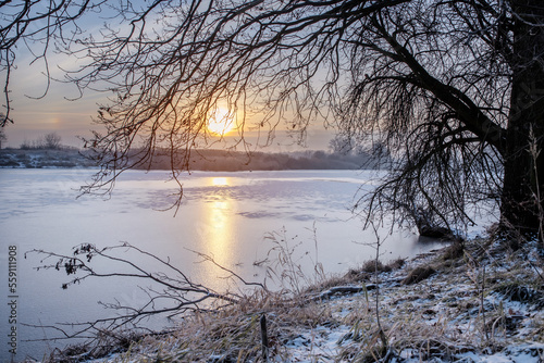 Krajobraz zimowy. Widok ze wschodem słońca i zimowy poranek nad rzeką. Zamrożona rzeka. Świtanie w zimowej scenerii. Mroźny poranek. Tło natury. 