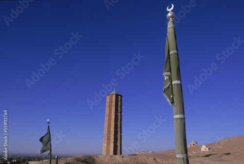 Green flags decorating a saint or holy man's tomb flutter below a towering brick minaret on the road into Ghazni, Afghanistan.