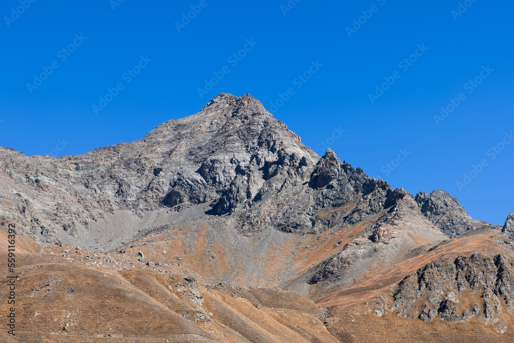 Impassable granite raven vertical mountainside and tipped rocks with black top peak under background of clear blue sky, Aosta valley, Italy