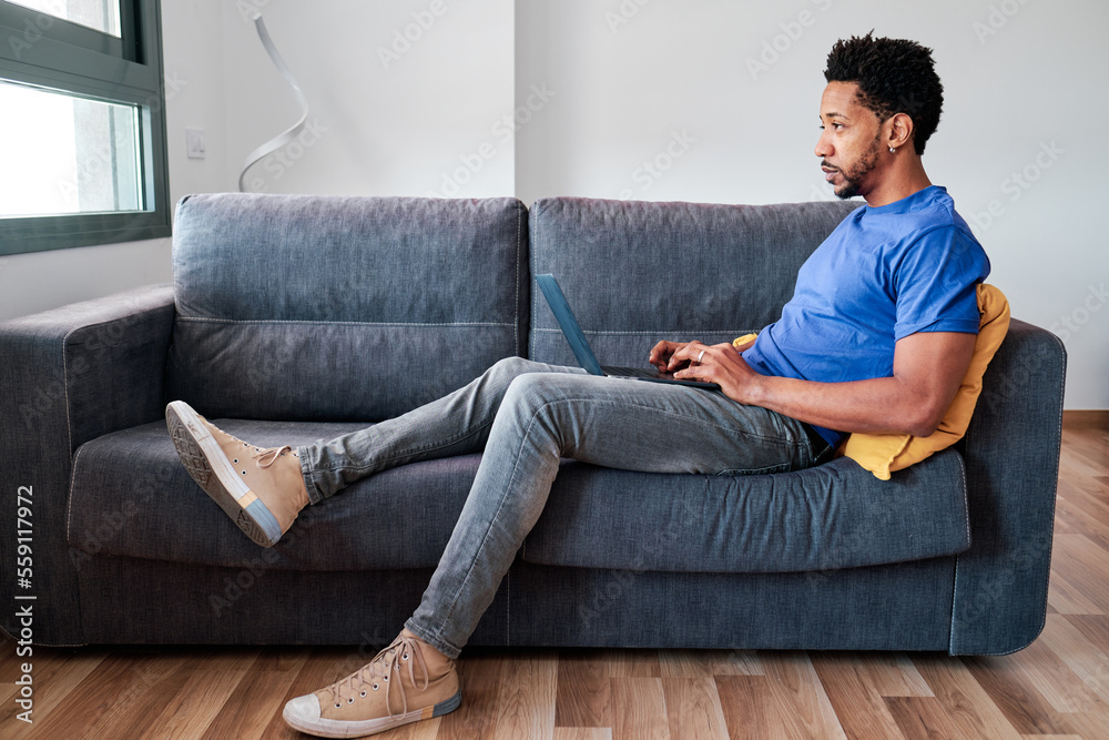 Man using a laptop while sitting on a sofa at home. Man using a laptop while sitting on a sofa at home.