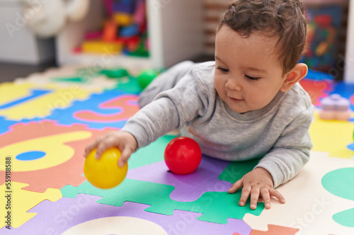 Adorable hispanic baby playing with balls lying on floor at kindergarten