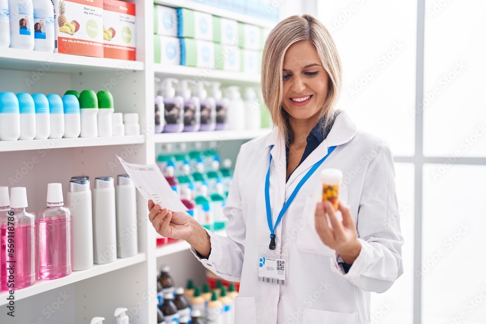 Young blonde woman pharmacist holding pills bottle reading prescription at pharmacy Young blonde woman pharmacist holding pills bottle reading prescription at pharmacy