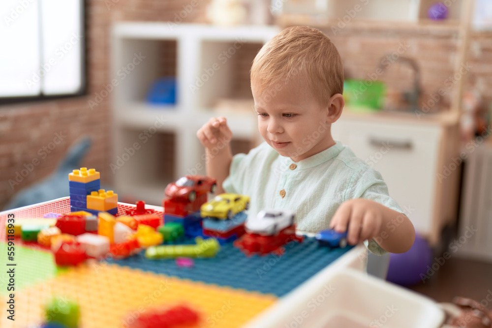 Adorable toddler playing with car and toy and construction blocks sitting on table at kindergarten Adorable toddler playing with car and toy and construction blocks sitting on table at kindergarten