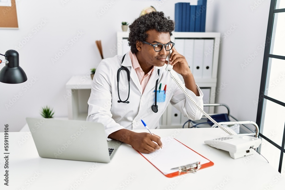 Young south east man wearing doctor uniform talking on the telephone at clinic Young south east man wearing doctor uniform talking on the telephone at clinic