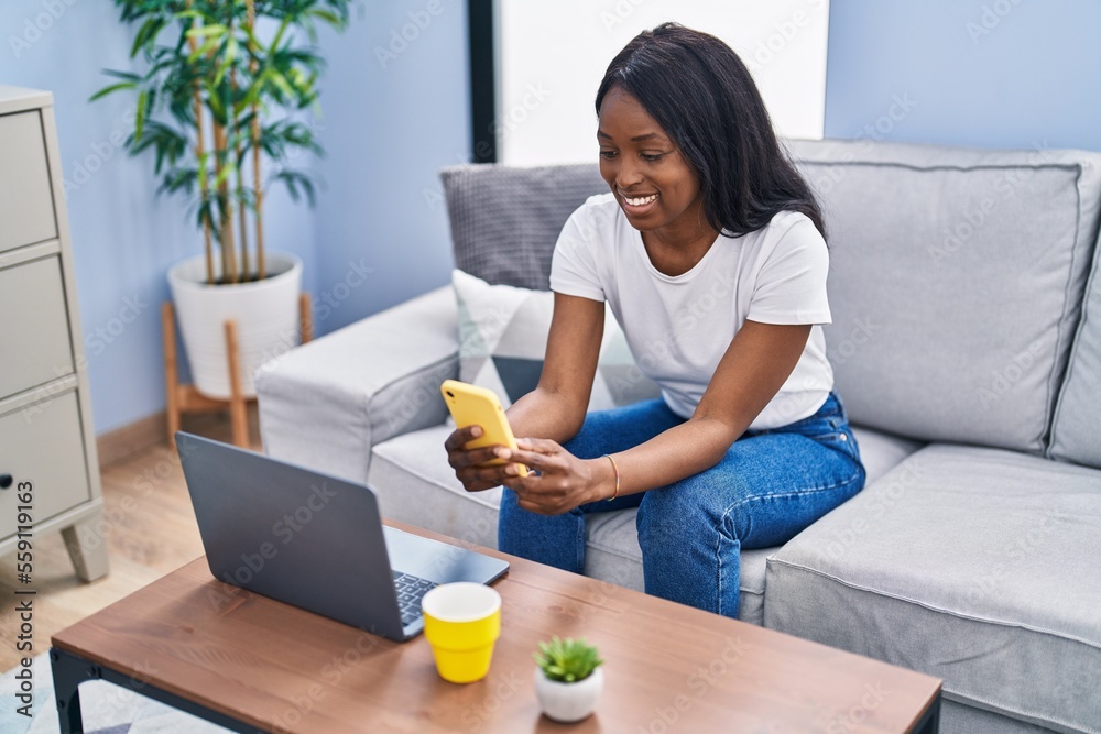 Young african american woman using laptop and smartphone at home
