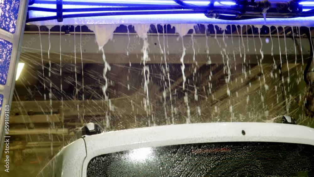 Automatic car wash at night. white car moves in pressure washer and