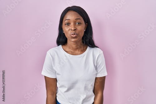 African young woman wearing casual white t shirt looking at the camera blowing a kiss on air being lovely and sexy. love expression.