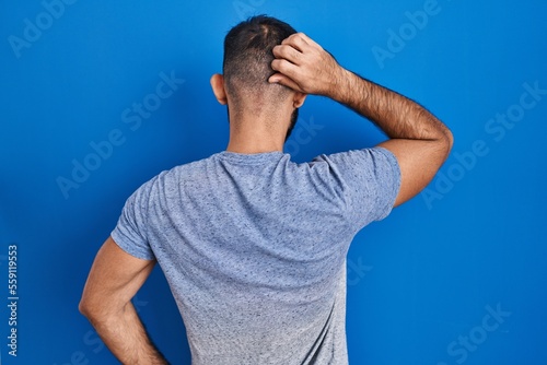 Middle east man with beard standing over blue background backwards thinking about doubt with hand on head