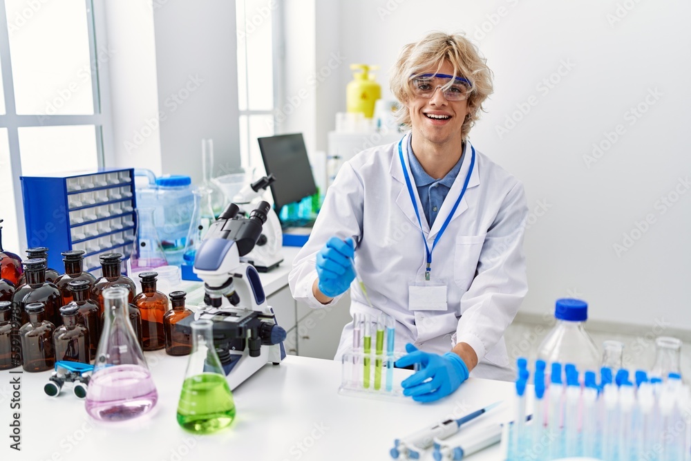 Fototapeta premium Young blond man scientist pouring liquid on test tube at laboratory