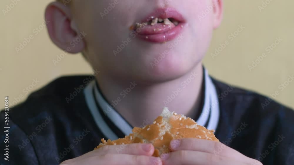 close-up caucasian boy 7 years old in defocus eats an appetizing burger, selective focus.child eats a burger in a cafe.fast food concept, food delivery close-up caucasian boy 7 years old in defocus eats an appetizing burger, selective focus.child eats a burger in a cafe.fast food concept, food delivery