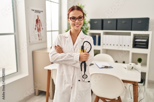 Young caucasian woman doctor standing with arms crossed gesture holding stethoscope at clinic
