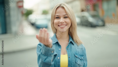 Young blonde woman smiling confident doing coming gesture with hand at street