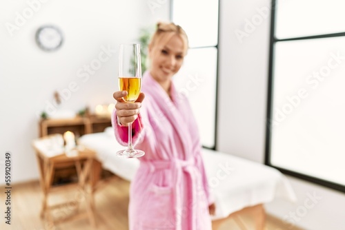 Young caucasian woman wearing bathrobe drinking champagne at beauty salon