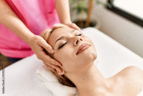 Young caucasian woman lying on table having head massage at beauty salon