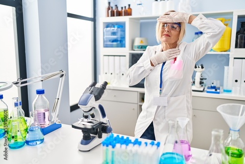 Middle age blonde woman working at scientist laboratory touching forehead for illness and fever  flu and cold  virus sick