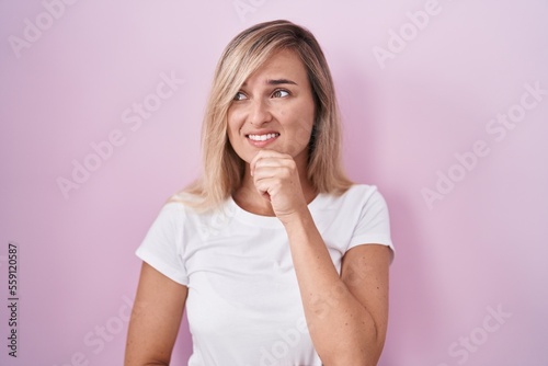 Young blonde woman standing over pink background thinking worried about a question, concerned and nervous with hand on chin