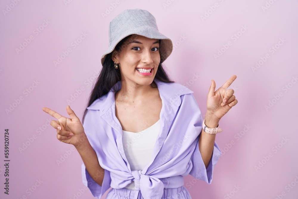Young hispanic woman standing over pink background wearing hat smiling confident pointing with fingers to different directions. copy space for advertisement Young hispanic woman standing over pink background wearing hat smiling confident pointing with fingers to different directions. copy space for advertisement