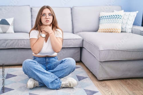 Young caucasian woman sitting on the floor at the living room shouting suffocate because painful strangle. health problem. asphyxiate and suicide concept.