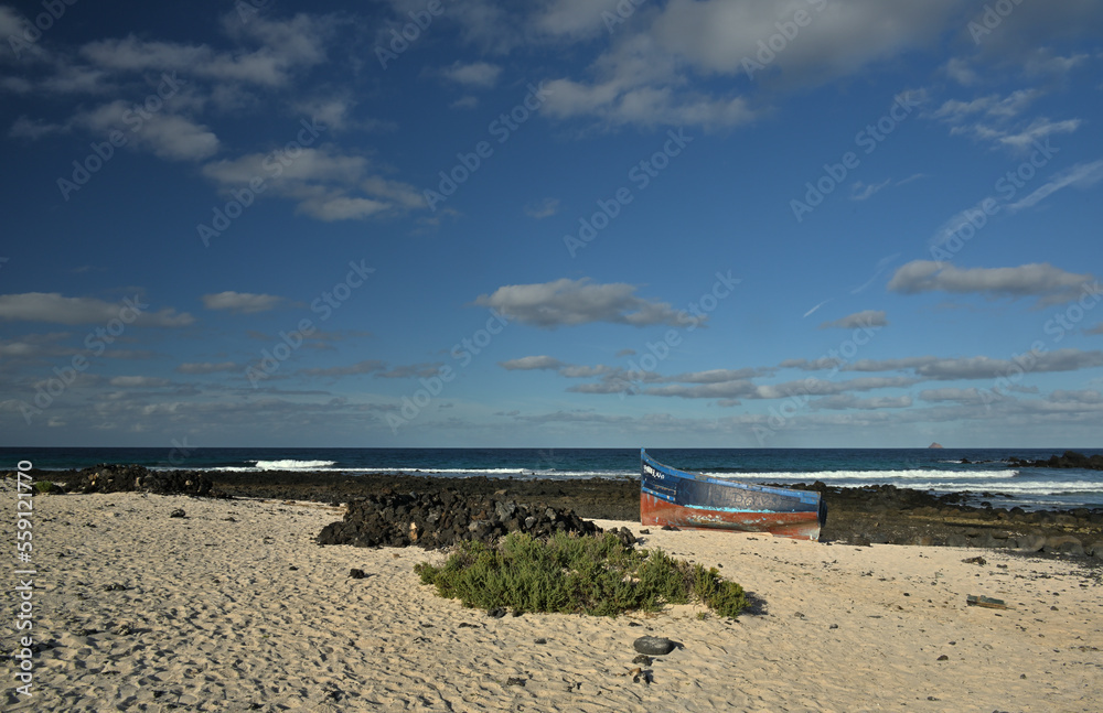 Ein Boot liegt an einem Sandstrand und im Hintergrund ist die felsige Küste und das Meer zu sehen.