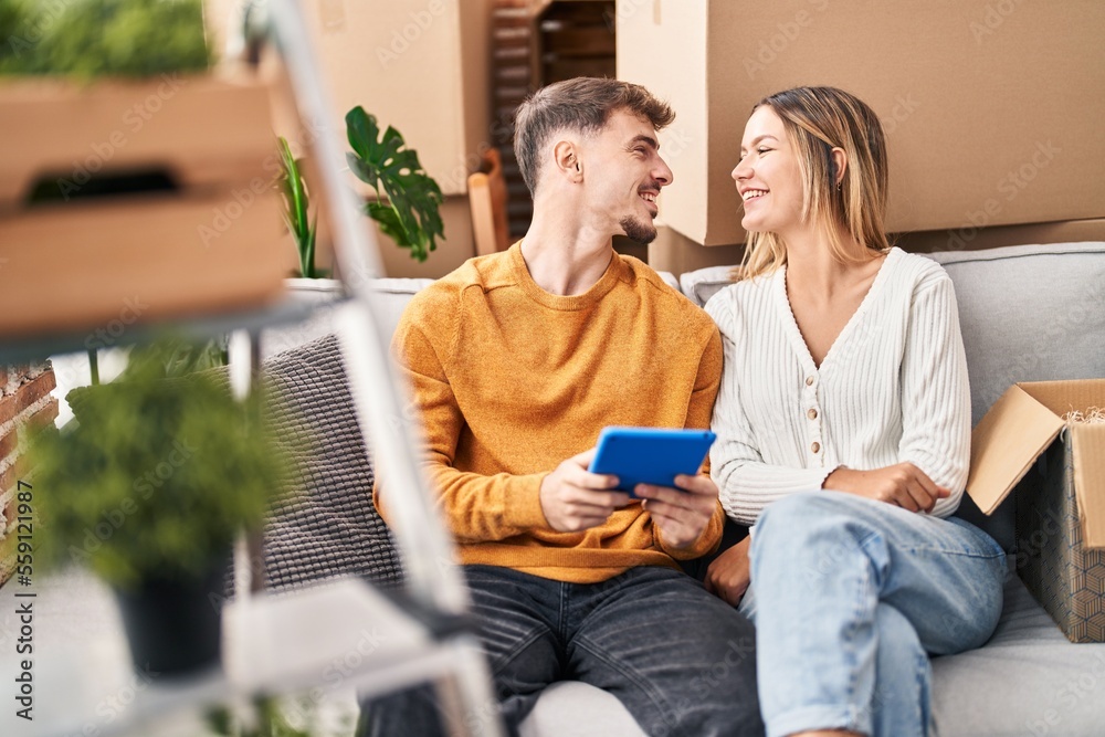 Young man and woman couple using touchpad sitting on sofa at new home