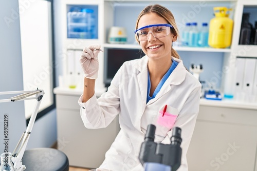 Young hispanic woman scientist holding sample with tweezer at laboratory