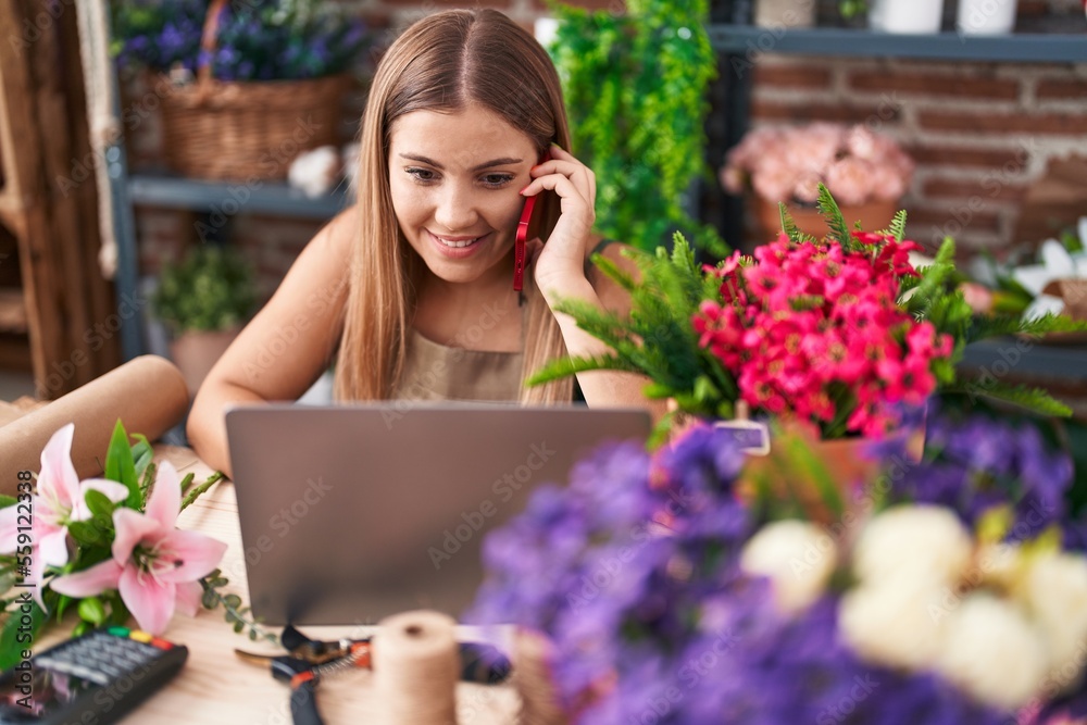 Young beautiful hispanic woman florist talking on smartphone using laptop at florist