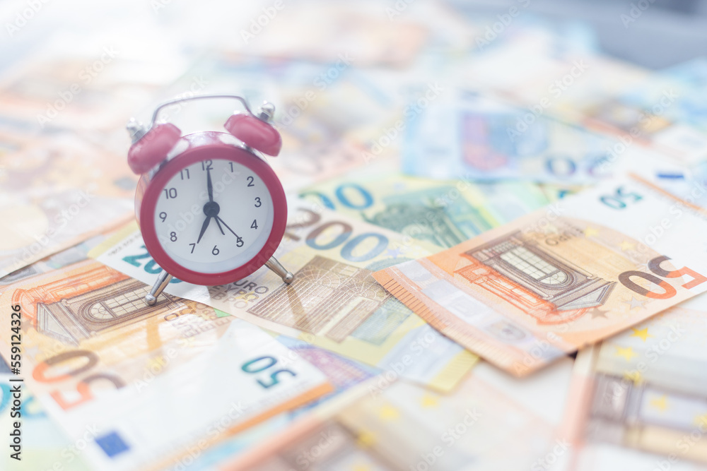 Red alarm clock and euro banknotes of various denominations on a white background. Red alarm clock and euro banknotes of various denominations on a white background.
