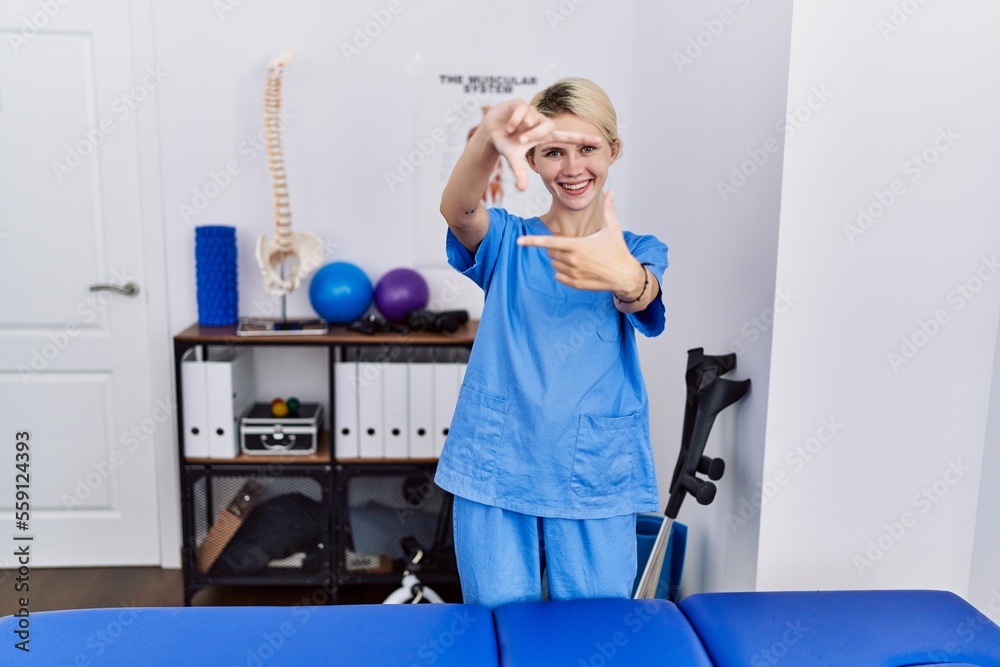Young physiotherapist woman working at pain recovery clinic smiling making frame with hands and fingers with happy face. creativity and photography concept. Young physiotherapist woman working at pain recovery clinic smiling making frame with hands and fingers with happy face. creativity and photography concept.