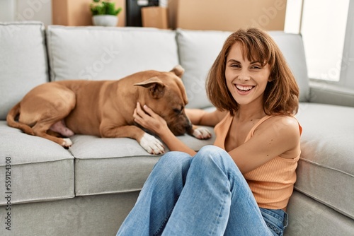 Young caucasian woman hugging dog sitting on floor at home