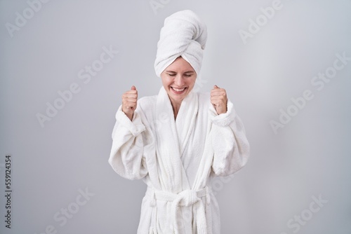 Blonde caucasian woman wearing bathrobe excited for success with arms raised and eyes closed celebrating victory smiling. winner concept.