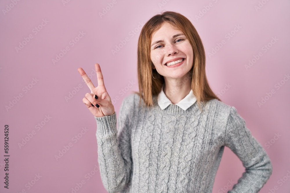 Beautiful woman standing over pink background smiling looking to the camera showing fingers doing victory sign. number two. Beautiful woman standing over pink background smiling looking to the camera showing fingers doing victory sign. number two.