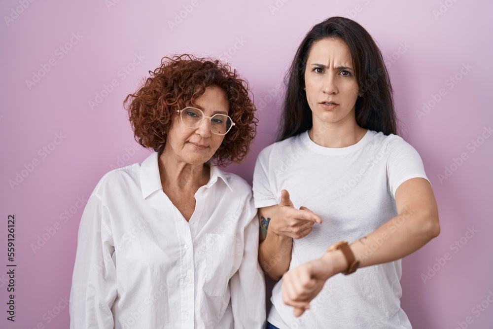 Hispanic mother and daughter wearing casual white t shirt over pink background in hurry pointing to watch time, impatience, upset and angry for deadline delay