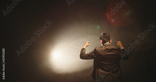 Rear view of male music conductor holding baton against black background photo