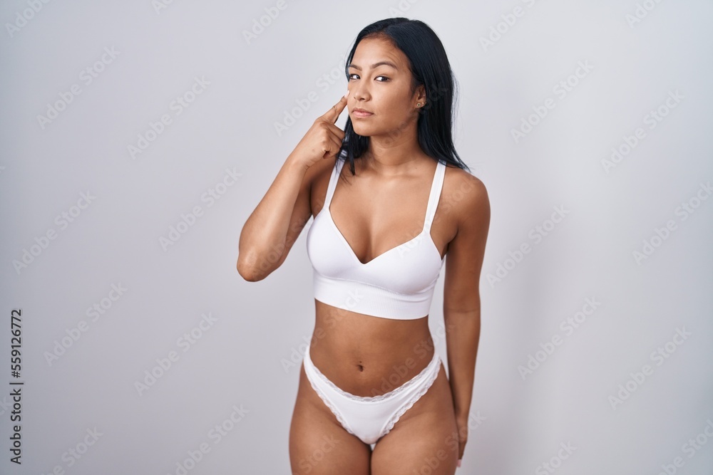 Hispanic woman wearing lingerie pointing to the eye watching you gesture, suspicious expression Hispanic woman wearing lingerie pointing to the eye watching you gesture, suspicious expression