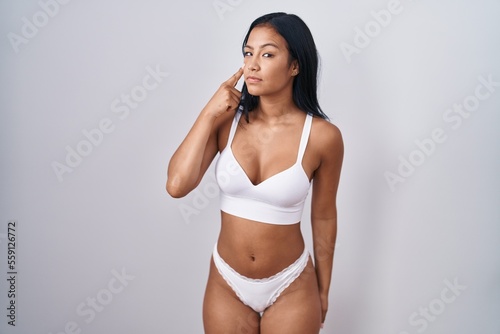 Hispanic woman wearing lingerie pointing to the eye watching you gesture, suspicious expression