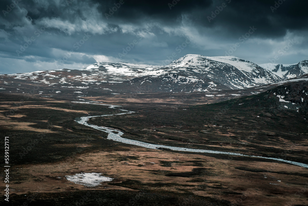 River Leirungsae with snow covered mountains in Jotunheimen National Park in Norway from above, dark clouds in sky