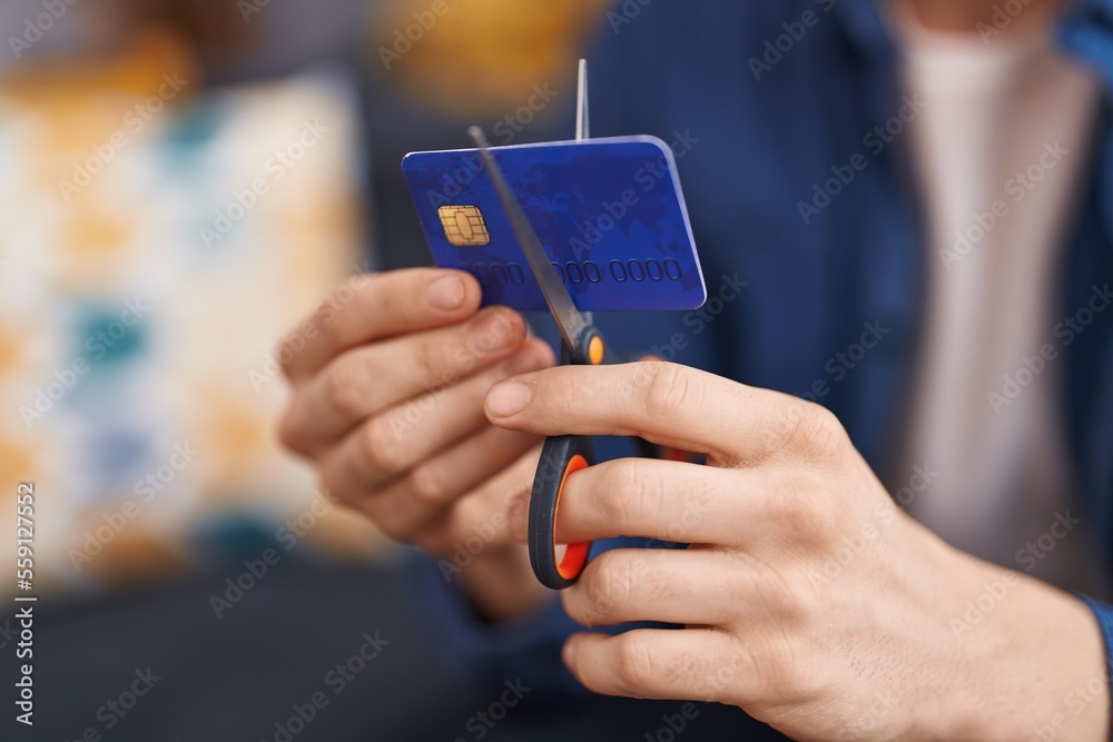 Young caucasian man cutting credit card sitting on sofa at home Young caucasian man cutting credit card sitting on sofa at home