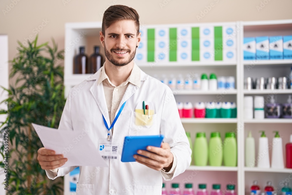 Young caucasian man pharmacist using touchpad reading prescription at pharmacy Young caucasian man pharmacist using touchpad reading prescription at pharmacy