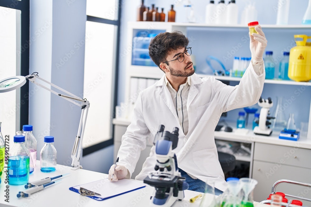 Young hispanic man scientist writing on document holding urine test tube at laboratory Young hispanic man scientist writing on document holding urine test tube at laboratory