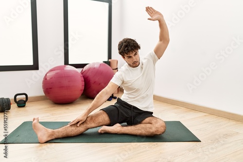 Young hispanic man stretching at sport center