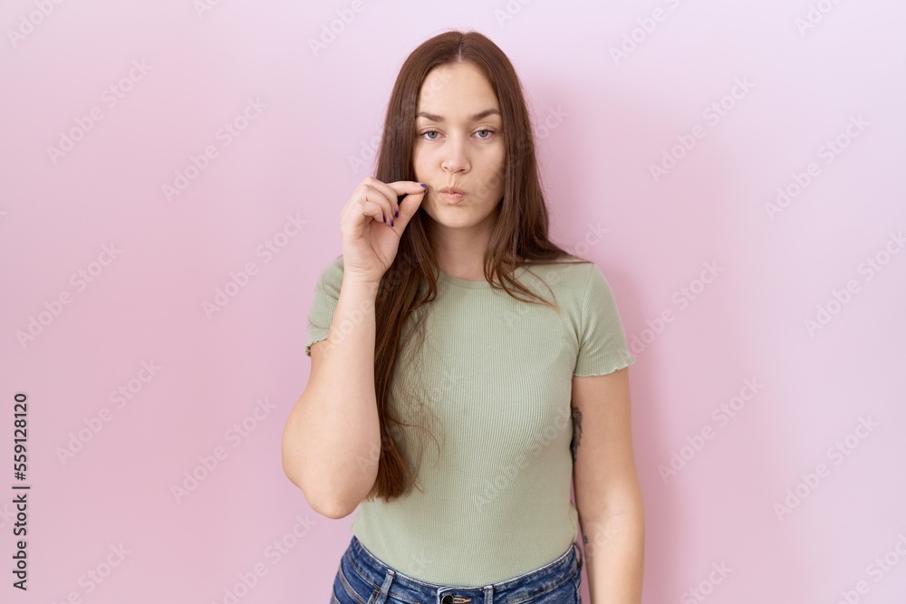 Beautiful brunette woman standing over pink background mouth and lips shut as zip with fingers. secret and silent, taboo talking Beautiful brunette woman standing over pink background mouth and lips shut as zip with fingers. secret and silent, taboo talking
