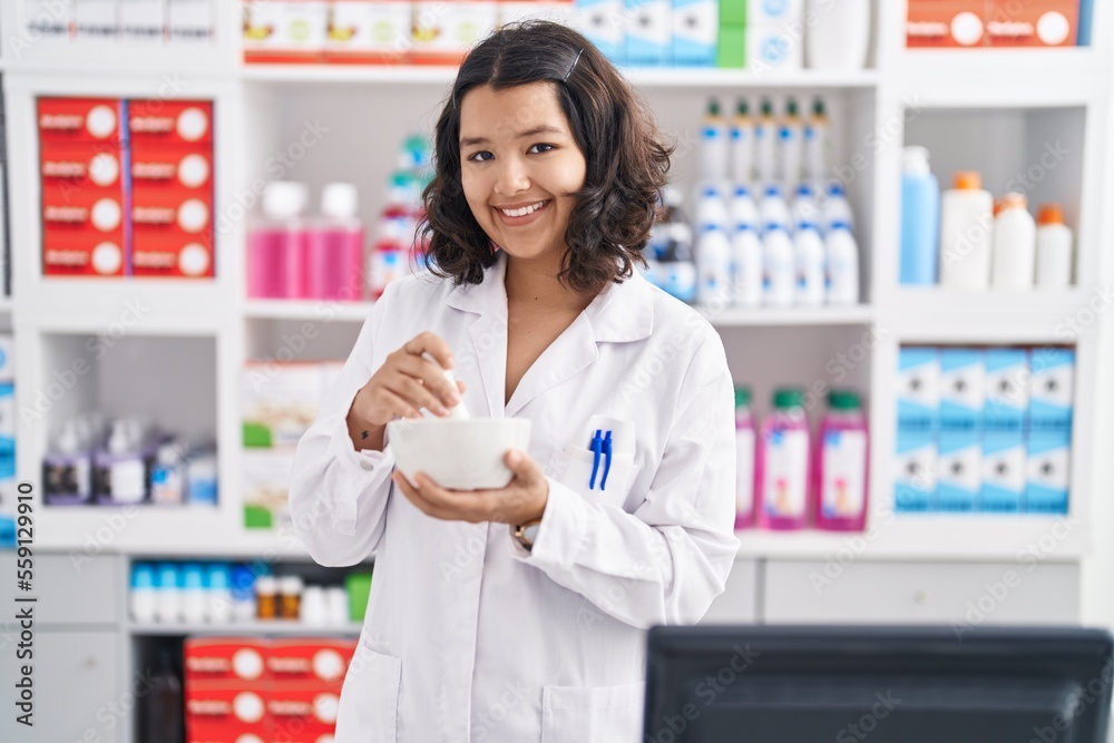 Young woman pharmacist smiling confident mixing medicine at pharmacy