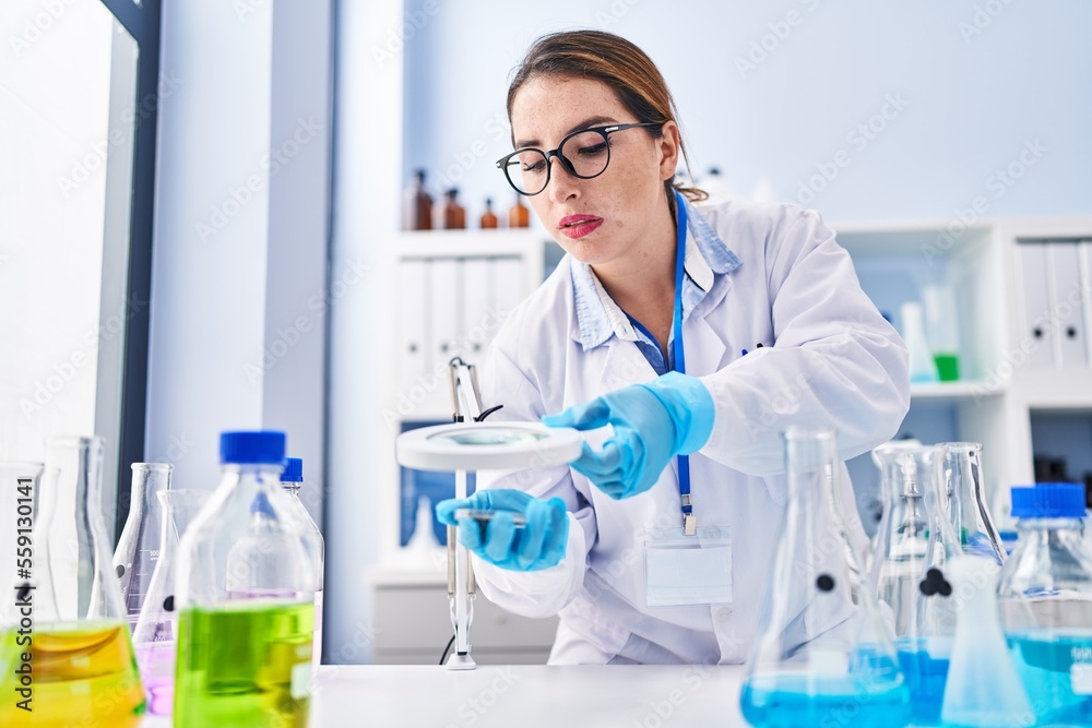Young beautiful hispanic woman scientist using magnifying glass at laboratory Young beautiful hispanic woman scientist using magnifying glass at laboratory