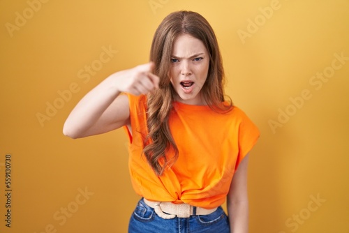Caucasian woman standing over yellow background pointing displeased and frustrated to the camera, angry and furious with you