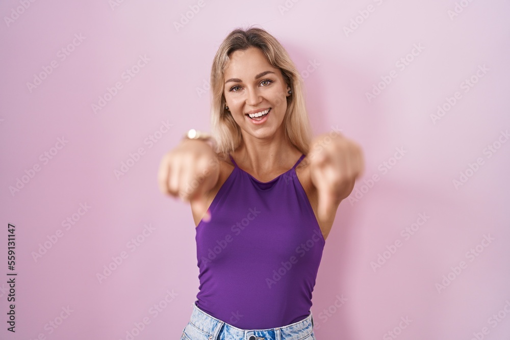 Young blonde woman standing over pink background pointing to you and the camera with fingers, smiling positive and cheerful Young blonde woman standing over pink background pointing to you and the camera with fingers, smiling positive and cheerful