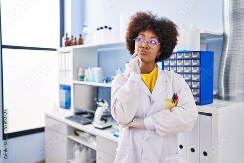 Fototapeta Naklejka Na Ścianę i Meble -  Young african american woman working at scientist laboratory thinking concentrated about doubt with finger on chin and looking up wondering