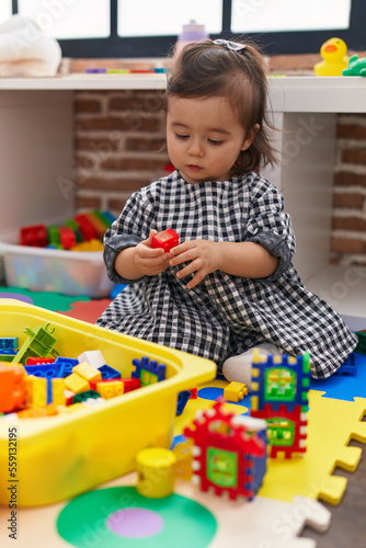 Adorable chinese girl playing with construction blocks sitting on floor at kindergarten