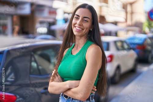 Young beautiful hispanic woman standing with arms crossed gesture at street